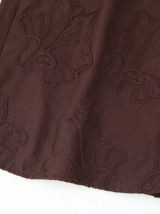 Gros plan détaillé d'une broderie florale marron foncé sur un tissu tissé de qualité