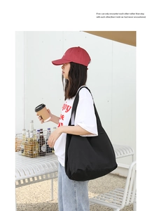 Close-up of a large black canvas tote bag with wide straps in an outdoor casual setting
