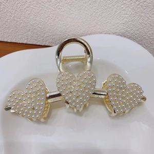 Detailed view of elegant golden heart-shaped hair claw clip with faux pearls and rhinestones