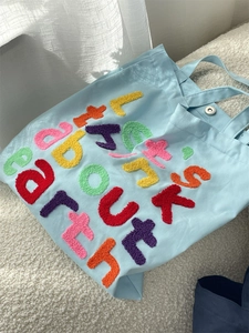 Detail of colorful fuzzy letter embroidery on a light blue canvas tote bag surface