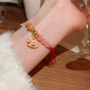 Détail du bracelet tressé rouge avec des perles roses et un pendentif cheval doré