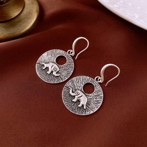 Détail macro des boucles d'oreilles éléphant vintage sur velours rouge foncé