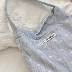 Gros plan d'un sac à bandoulière en velours bleu clair avec motif de cœurs blancs