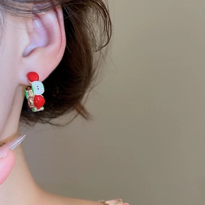 Detail view of a model wearing C-shaped red and green fruit earrings with a silver needle