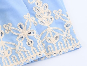 Close-up of intricate white eyelet embroidery on a light blue linen vacation dress