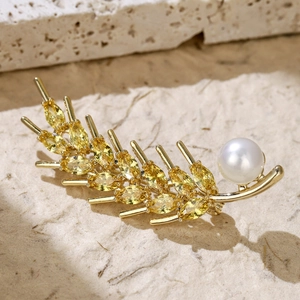 Macro detail of golden feather brooch with yellow zircon stones and a white pearl