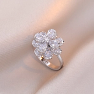 Bague trèfle rotative élégante avec zircons brillants sur un fond de soie beige