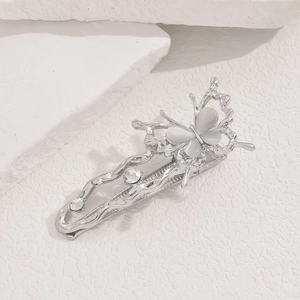 Macro shot of a silver butterfly hair clip with inlaid white gemstones on stone background
