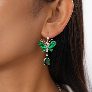 Close-up of green crystal butterfly earrings with teardrop pendants on model