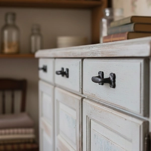 Vintage black cast iron pull handle installed on a white rustic wooden cabinet door