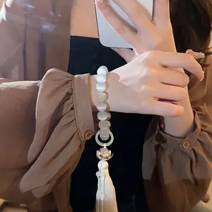 Elegant cat's eye stone beaded bracelet with lotus flower charm and white tassel on wrist