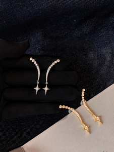Detail of silver and gold starburst dangle earrings with micro-pave crystals on denim