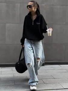 Street style view of a black quarter-zip sweatshirt paired with distressed blue jeans
