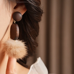 Close-up of retro earrings with dark brown wood beads and beige pom poms on model