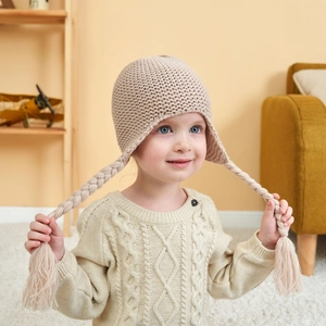 Detailed knit texture and long braided earflaps on a cozy beige baby winter hat