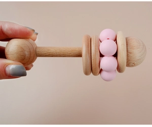 Detail of hand holding a pink silicone and beech wood baby rattle for easy grip and teething