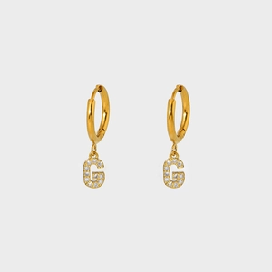 Close-up of gold-plated hoop earrings with G-letter pendant inlaid with white zircons