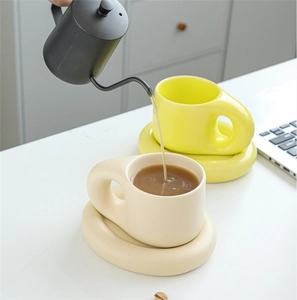 Action shot of coffee pouring into a chunky ceramic mug with a thick round handle and saucer