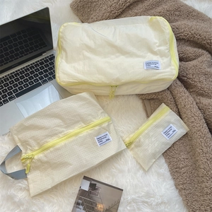 Three-piece travel organizer set in cream nylon with grid texture and yellow zippers