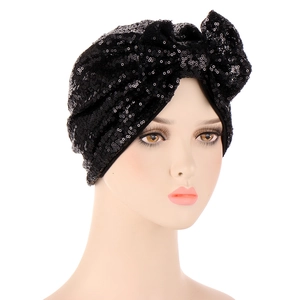 Detail of black turban hat with sequins and a large decorative bow on white background