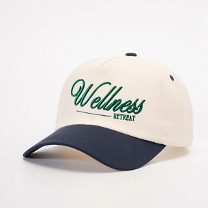 Detailed side view of beige and navy baseball cap with green Wellness Retreat embroidery