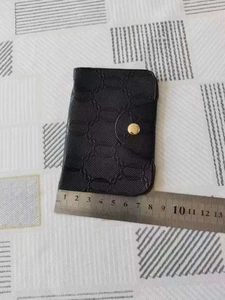 Macro shot of a black pebbled leather card holder showing detailed texture and gold button