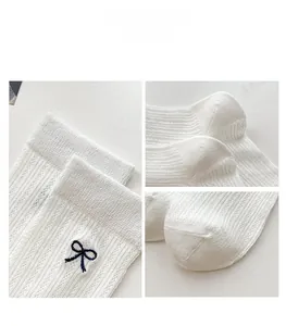 Close-up of white knitted slouch socks with navy blue bow embroidery and hollow stripes