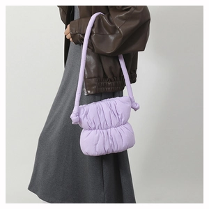 Detail view of the purple quilted nylon puffy bucket bag worn on the shoulder by a model