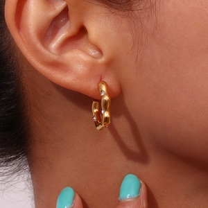 Detailed view of irregular wave gold-plated hoop earring with clear cubic zirconia stones