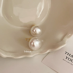 Detail of 14mm pearl earring on beige ceramic tray showing soft lustrous white finish