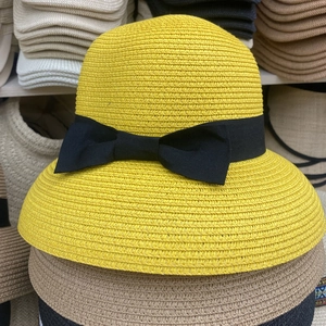 Detail of yellow straw sun hat featuring a delicate black ribbon bow and woven texture