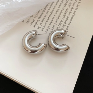 Detailed view of chunky C-shaped hoop earrings in polished silver on artistic book pages