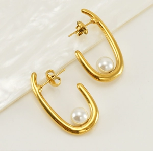 Détail macro de boucles d'oreilles en U dorées avec perles minimalistes sur fond blanc lisse