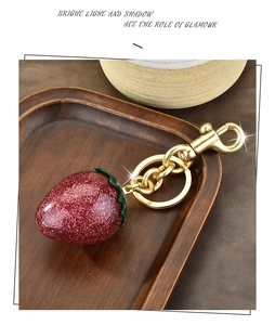 Close-up of a sparkling red strawberry keychain with gold hardware on a wooden tray