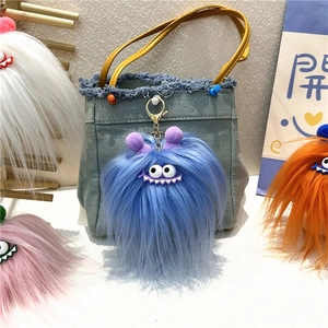 Blue fuzzy monster keychain with large eyes and metal clip hanging on a denim bag