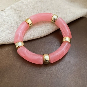 Detail view of pink marble resin tube beads and gold metal spacers on an elastic bracelet
