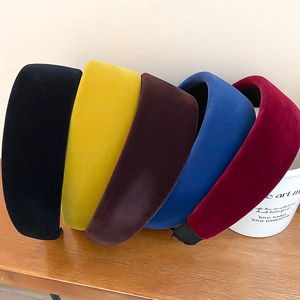 Five velvet padded headbands in black, yellow, brown, blue, and red on a wood surface