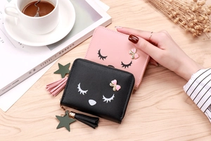 Detail of compact zip coin purse with eyelash pattern, glitter bow, and tassel charm