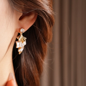 Close-up of elegant gold and white leaf earrings featuring clear zircon studs on model