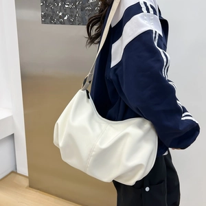 Minimalist white pleated dumpling bag worn by model in a modern indoor lifestyle setting