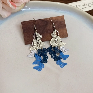 Detail of blue and white hollow butterfly tassel earrings on a wooden stand