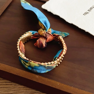 Detail view of a matte gold cuff bracelet featuring a blue and yellow floral silk ribbon