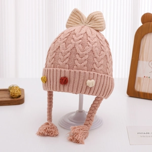 Dettaglio di un cappello da neonato in maglia rosa con un fiocco crema e treccine