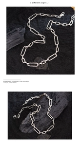 Detailed view of silver rectangular link chain necklace on textured black background