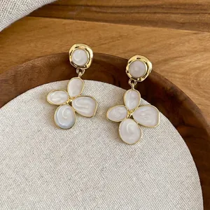 Détail de boucles d'oreilles fleuries avec pétales blancs et dorure sur plateau en bois