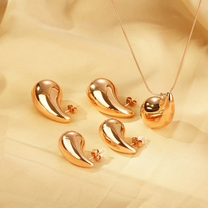 Detail shot of golden water drop pendant and matching earrings on soft beige fabric