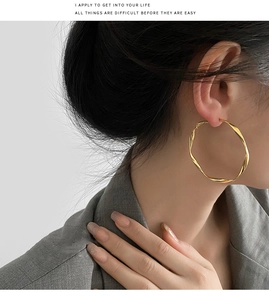 Macro detail of large twisted gold hoop earrings worn by a model in a grey suit