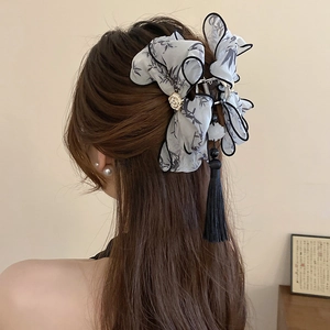 Detail of silk bow hair claw with gold rose and long tassels on dark hair