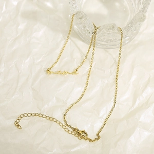 Gros plan du pendentif Mama doré sur une fine chaîne sur fond texturé blanc