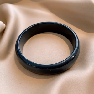 Detailed view of dark resin bangle with polished finish on elegant silk fabric
